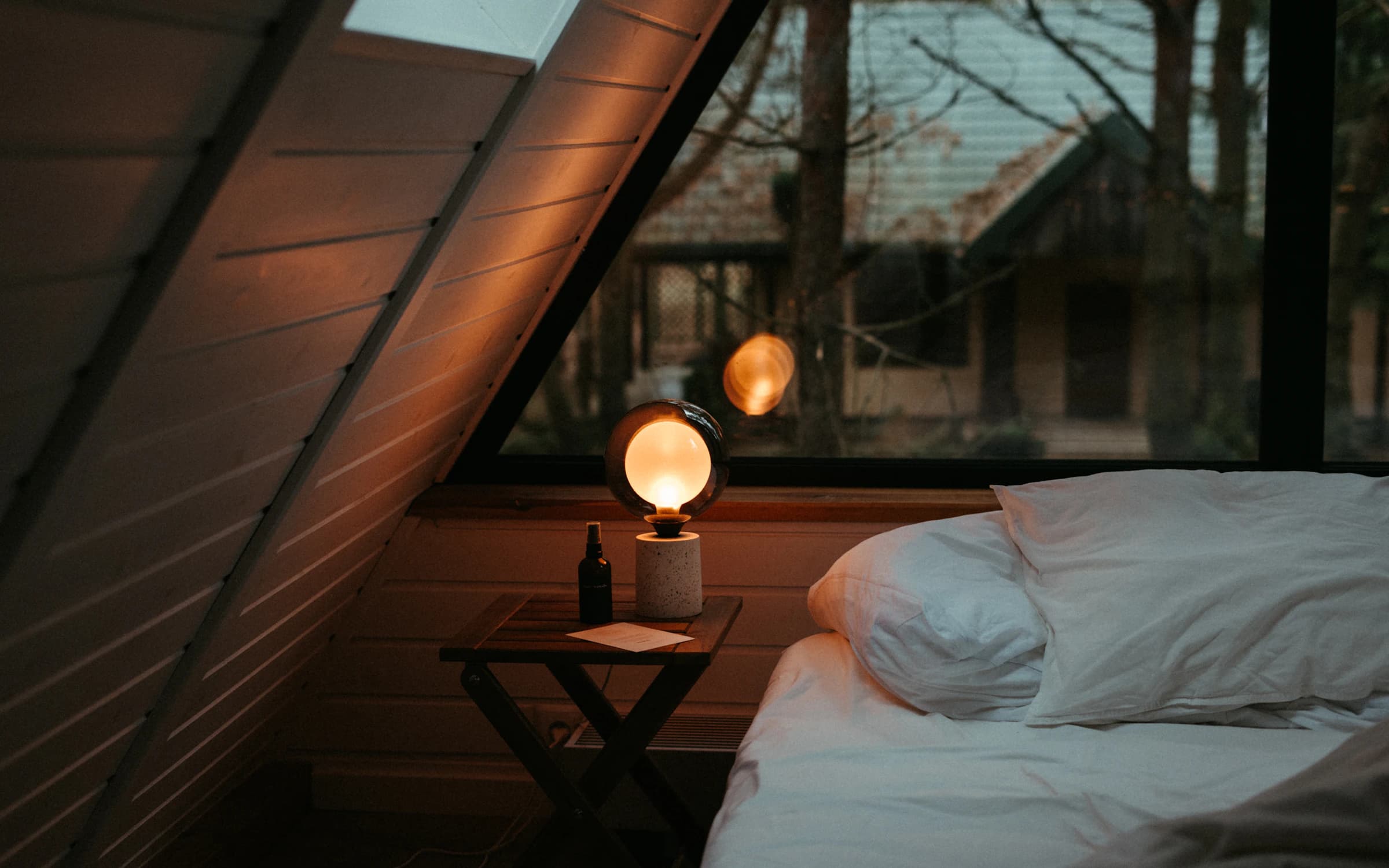 Schlafzimmer-Detail, Morgenlicht durchs Fenster, weiße Bettwäsche.